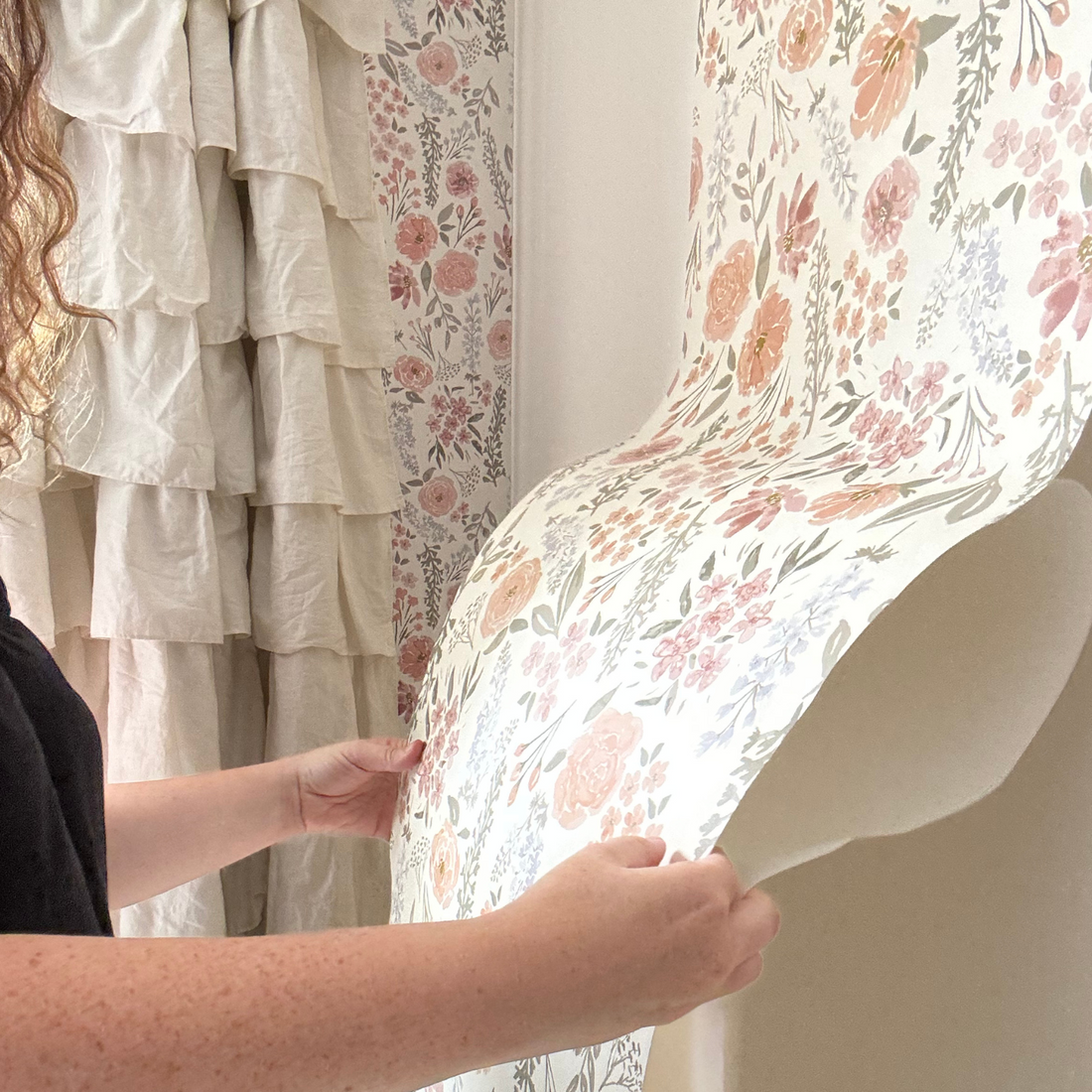 Person holding a floral-patterned sheer curtain with ruffled curtains in the background