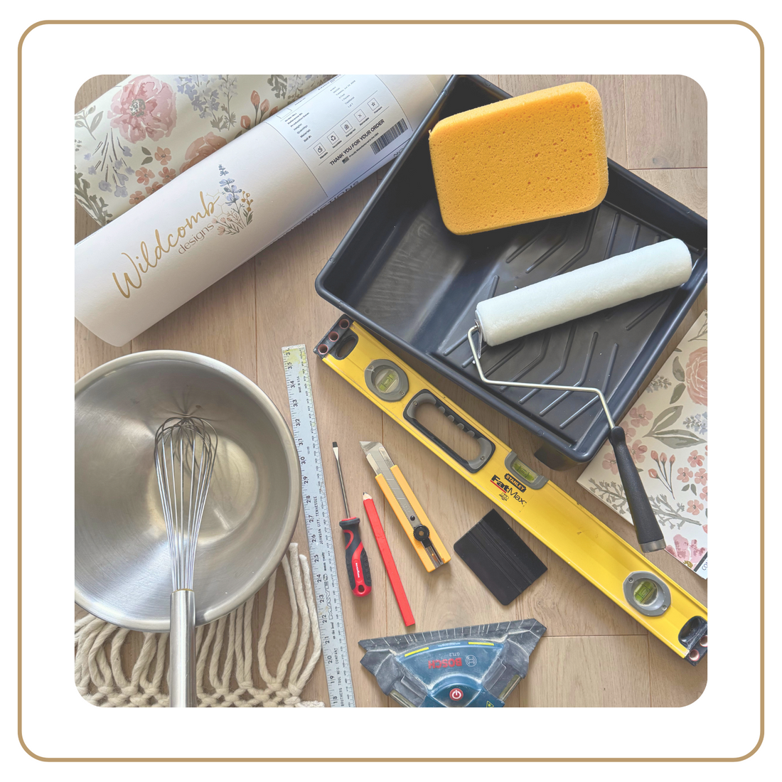 Set of painting tools including a roller, sponge, and measuring tape on a wooden surface.