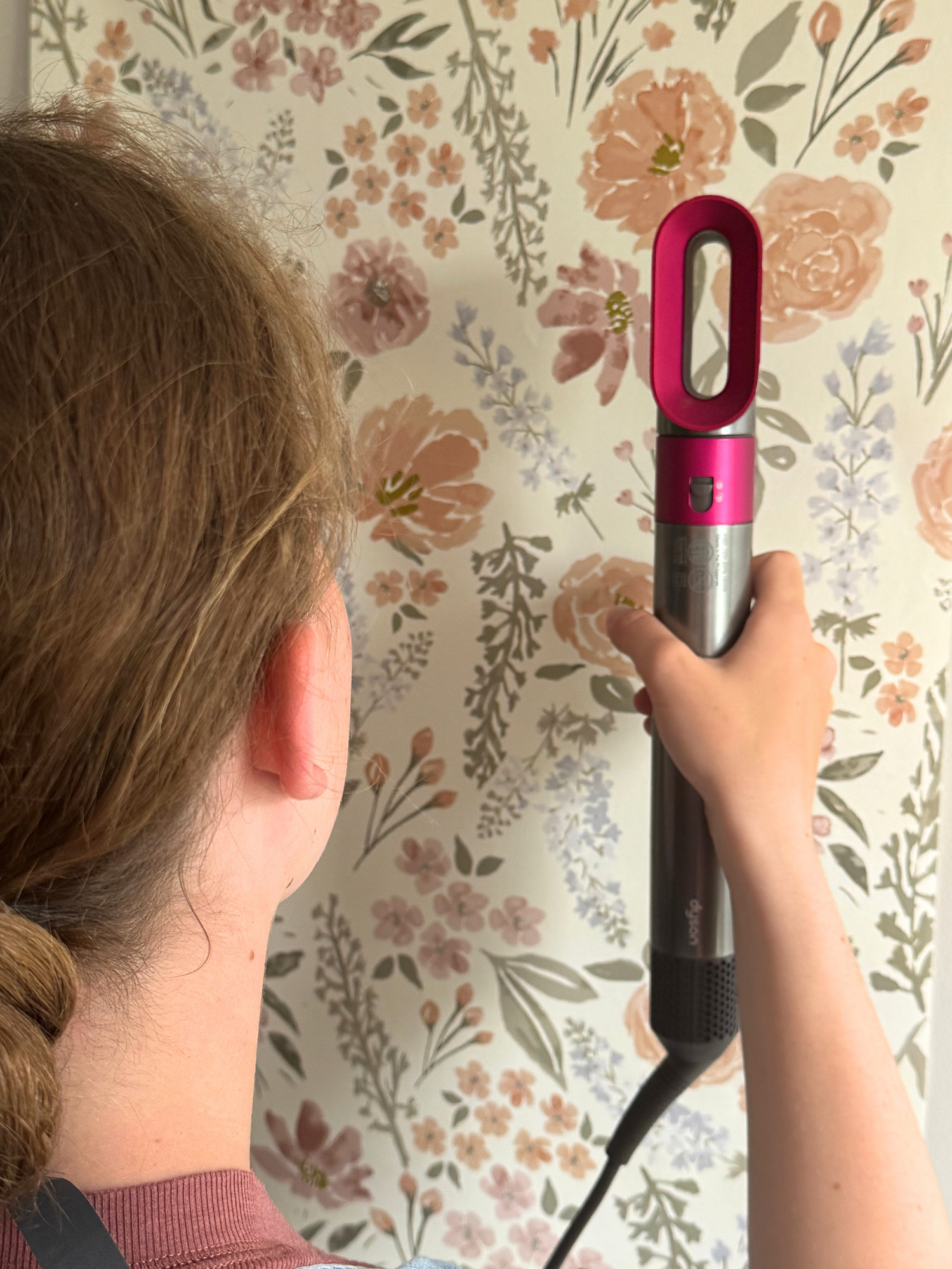 Person using a hair straightener against a floral wallpaper background