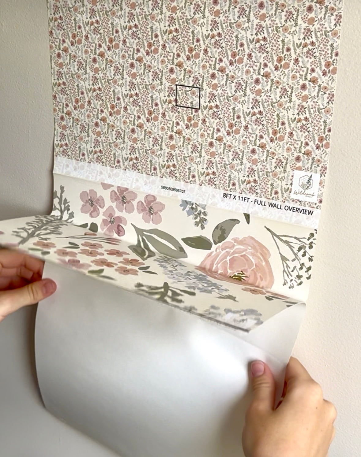 Floral wallpaper roll being unrolled with a person's hands visible.