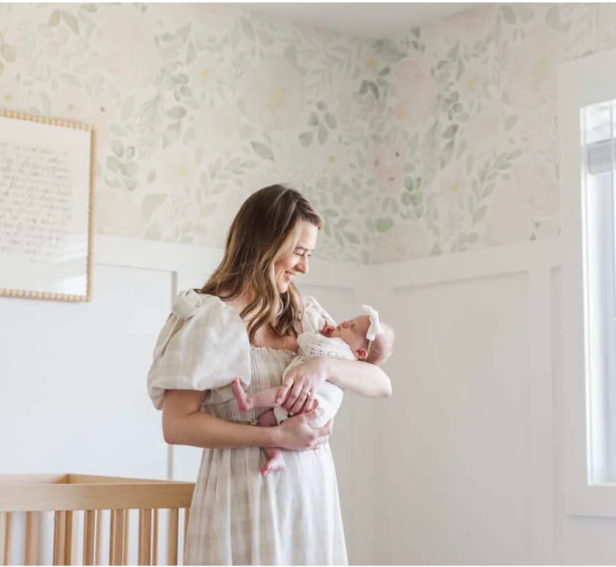 mom holding baby in a soft floral blush pink nursery with warm wood crib and panneling