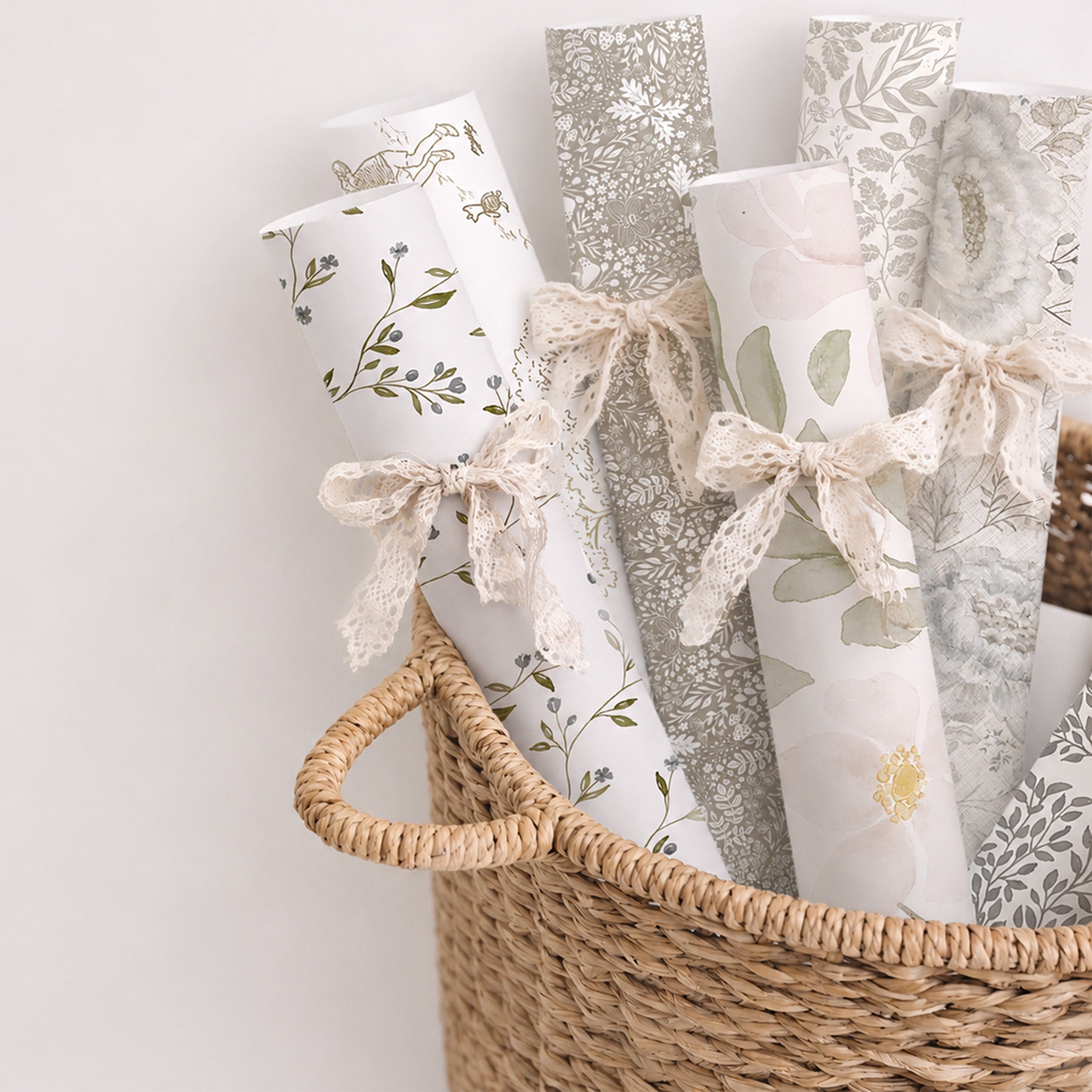 Wallpaper rolls featuring floral, woodland, and painterly designs styled in a woven basket with lace ribbon ties.