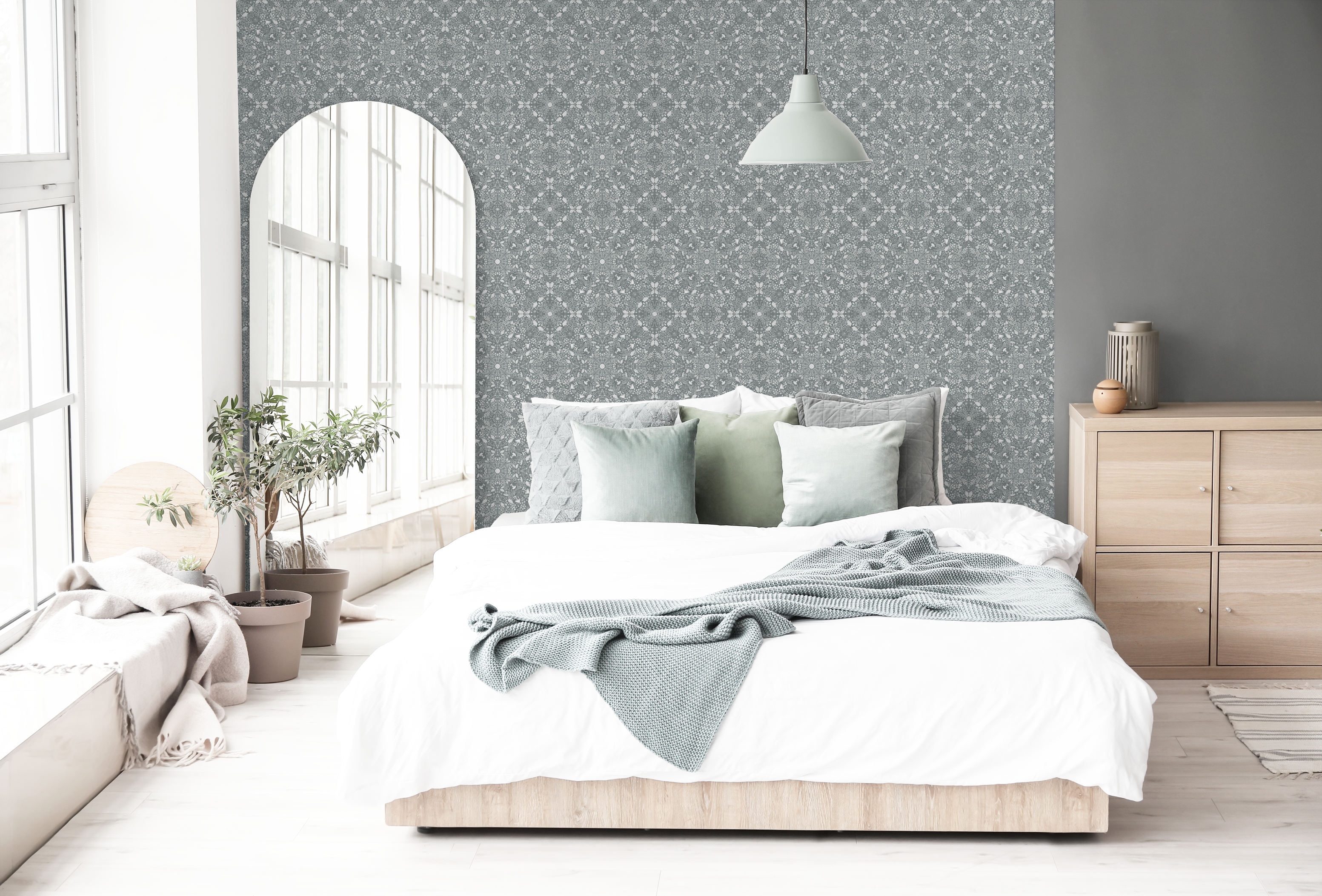 Calm bedroom with sage pillows, white bedding, and an arched floor mirror beside a wall covered in Woodland Lace in Blue wallpaper.