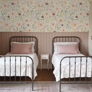 Two twin beds with iron frames against a floral wallpapered wall.
