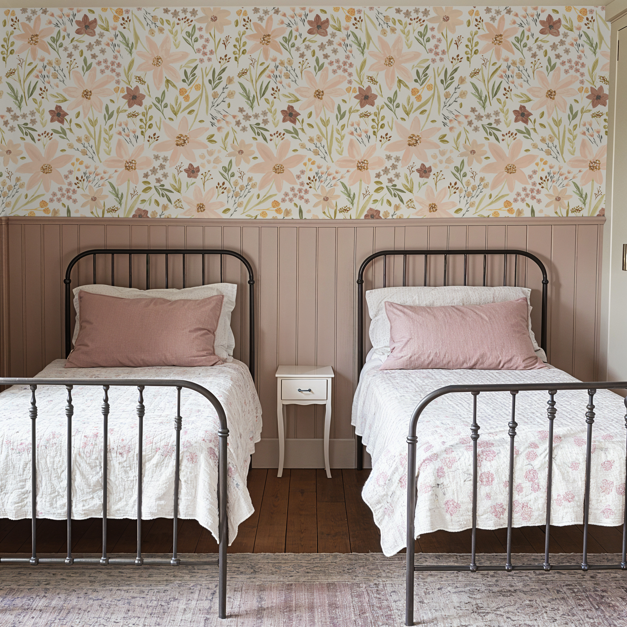 Two twin beds with iron frames against a floral wallpapered wall.