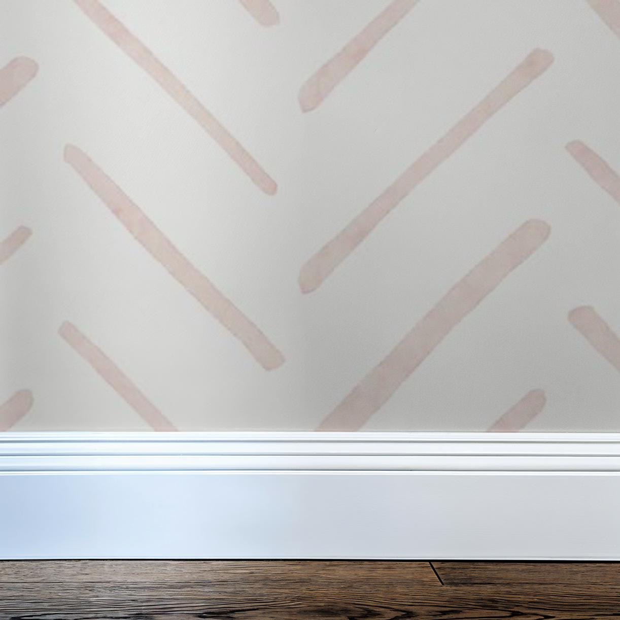 Close-up of blush pink watercolor herringbone wallpaper showing soft hand-painted lines above a white baseboard.