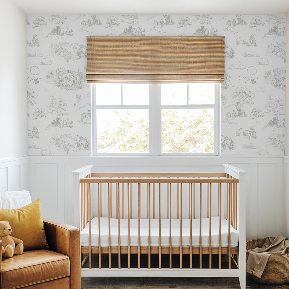 Sage Winnie the Pooh toile wallpaper in a bright nursery with white wall paneling, natural wood crib, and soft woven textures.