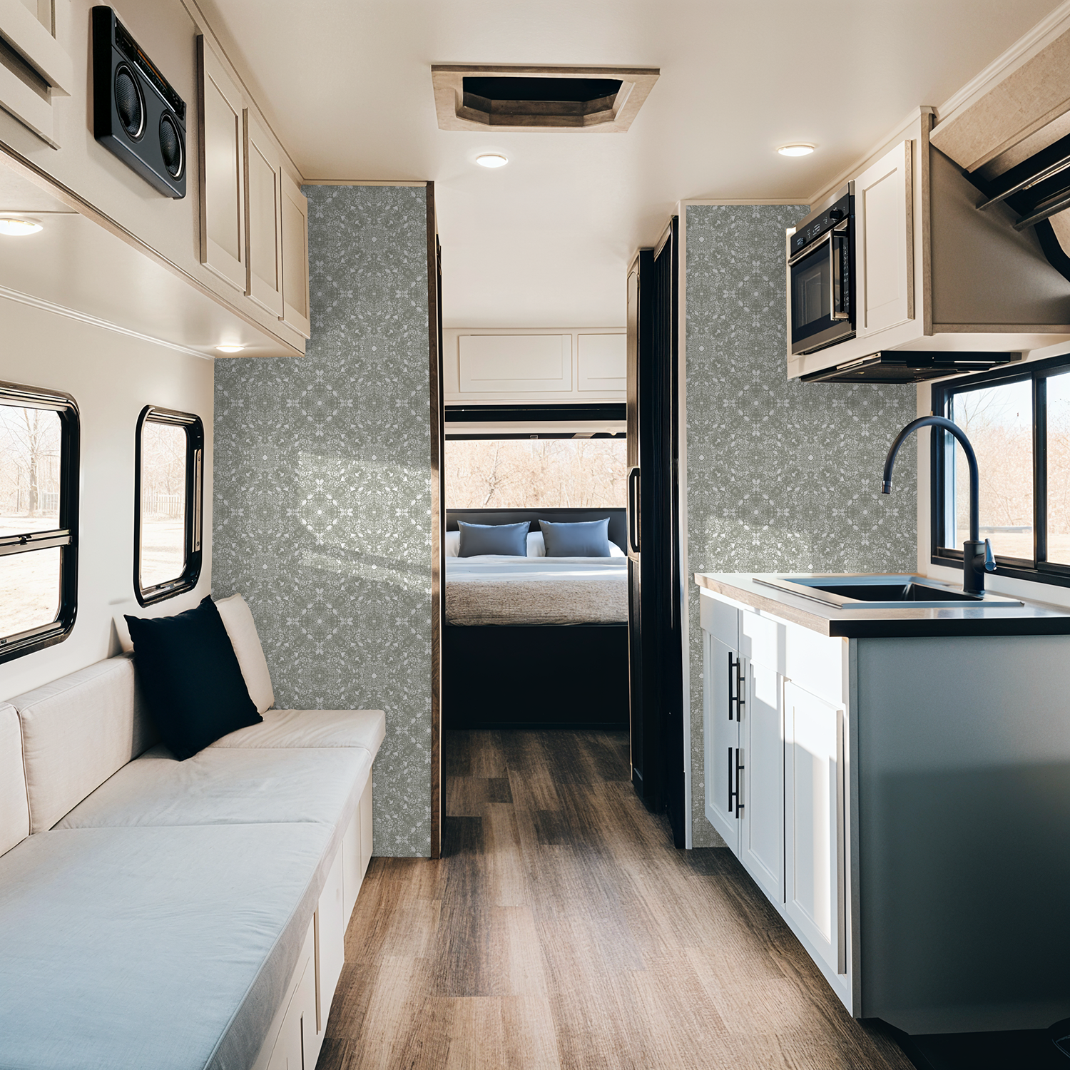 Modern RV interior with kitchen, living area, and bedroom in a Woodland Lace in Sage wallpaper.