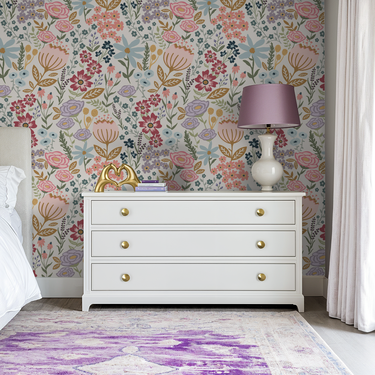 White dresser with lavender lamp and gold accents styled in front of Flo’s Vibrant Garden Party wallpaper with bold, colorful botanical pattern.