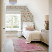 Neatly decorated bedroom with floral wallpaper, white bed, and pink rug.