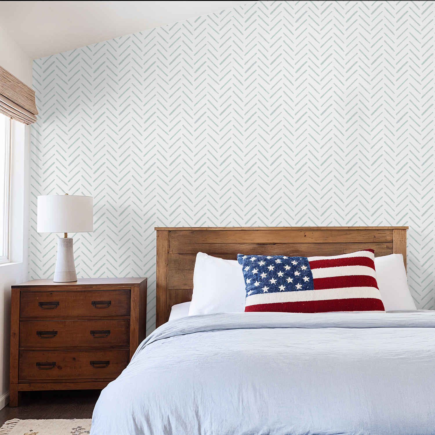 Blue watercolor chevron wallpaper in a rustic bedroom with a wooden headboard and American flag pillow.
