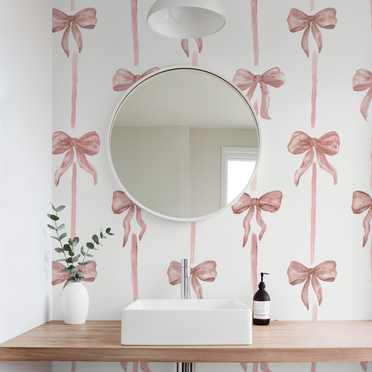 Bathroom with pink bow-patterned wallpaper, round mirror, sink, and decorative elements.