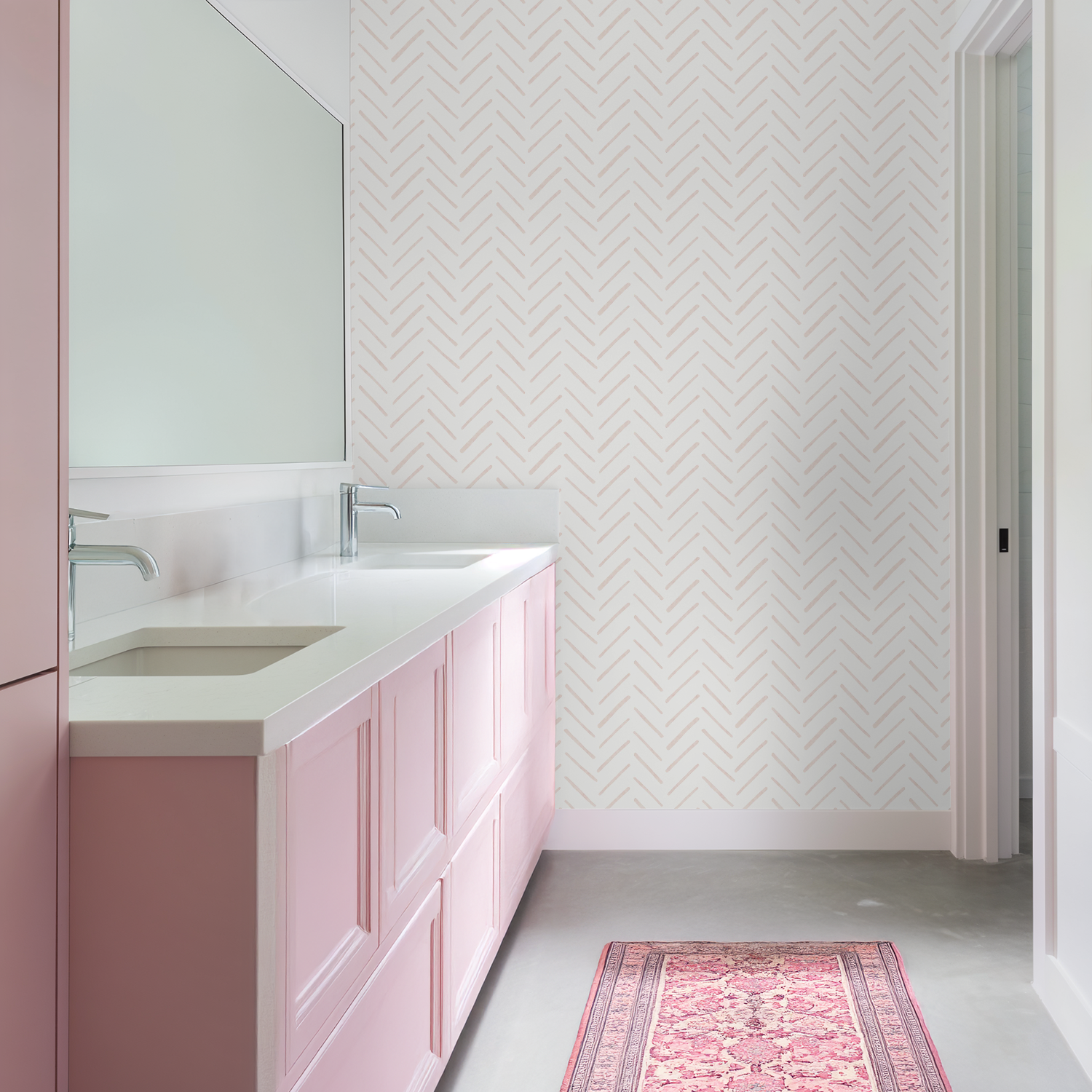 Blush pink watercolor herringbone wallpaper featured in a modern bathroom with soft pink cabinetry and a long white countertop.