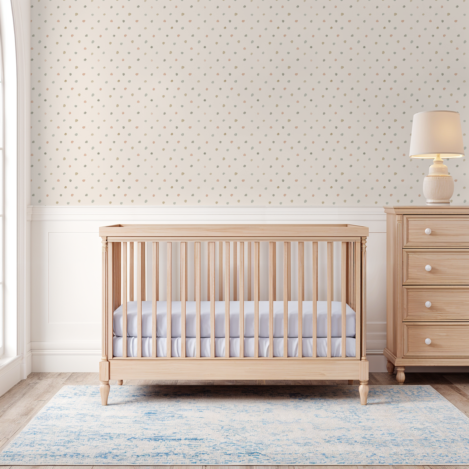 Wooden crib in a nursery with a lamp and dresser with dotted wallpaper