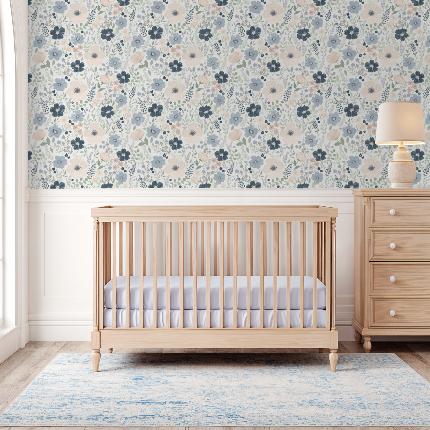 Navy and blush floral wallpaper behind a natural wood crib and dresser in a bright nursery with white molding.