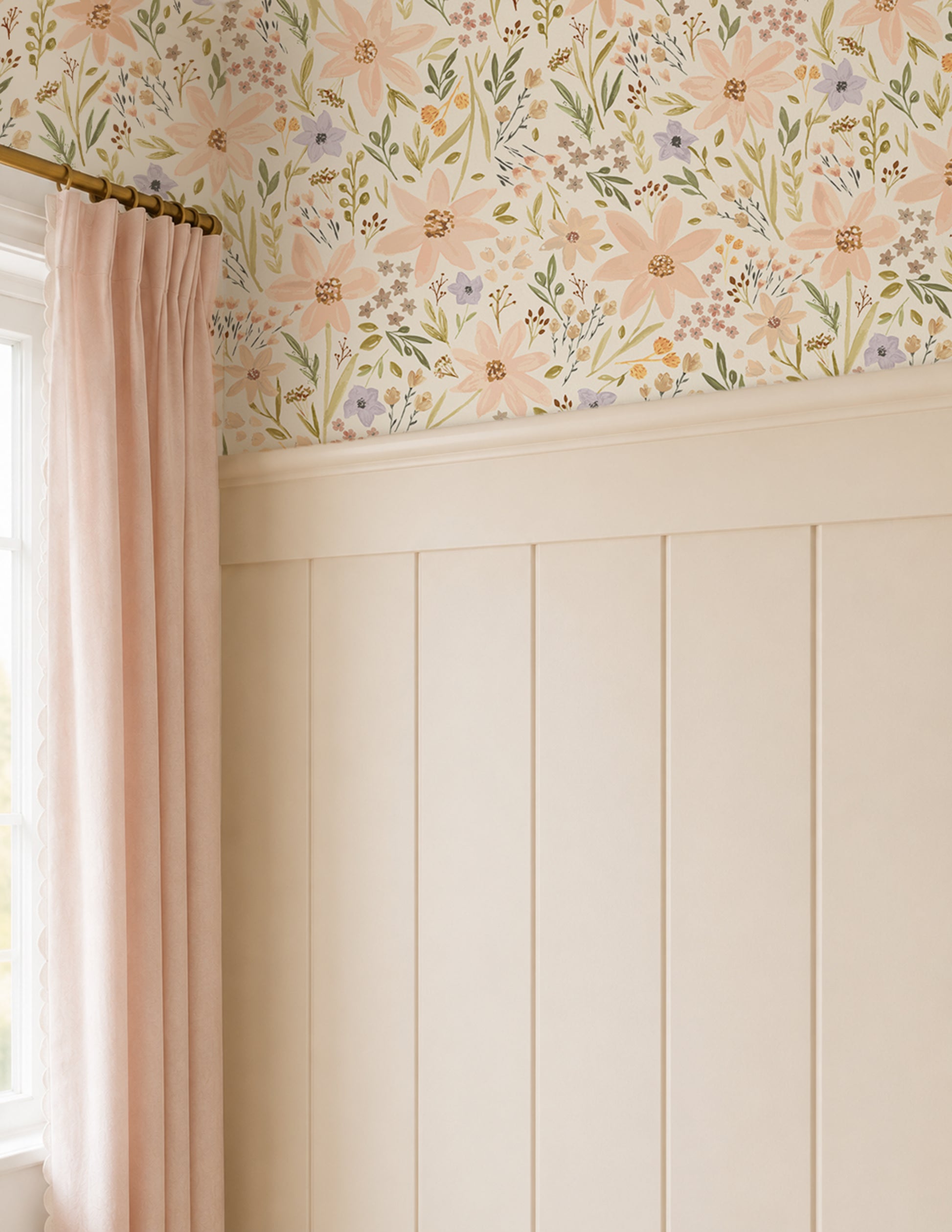 A styled interior corner showing floral wallpaper with large blush pink daisy flowers and green leaves above creamy white wainscoting, with a pink curtain hanging on the left.