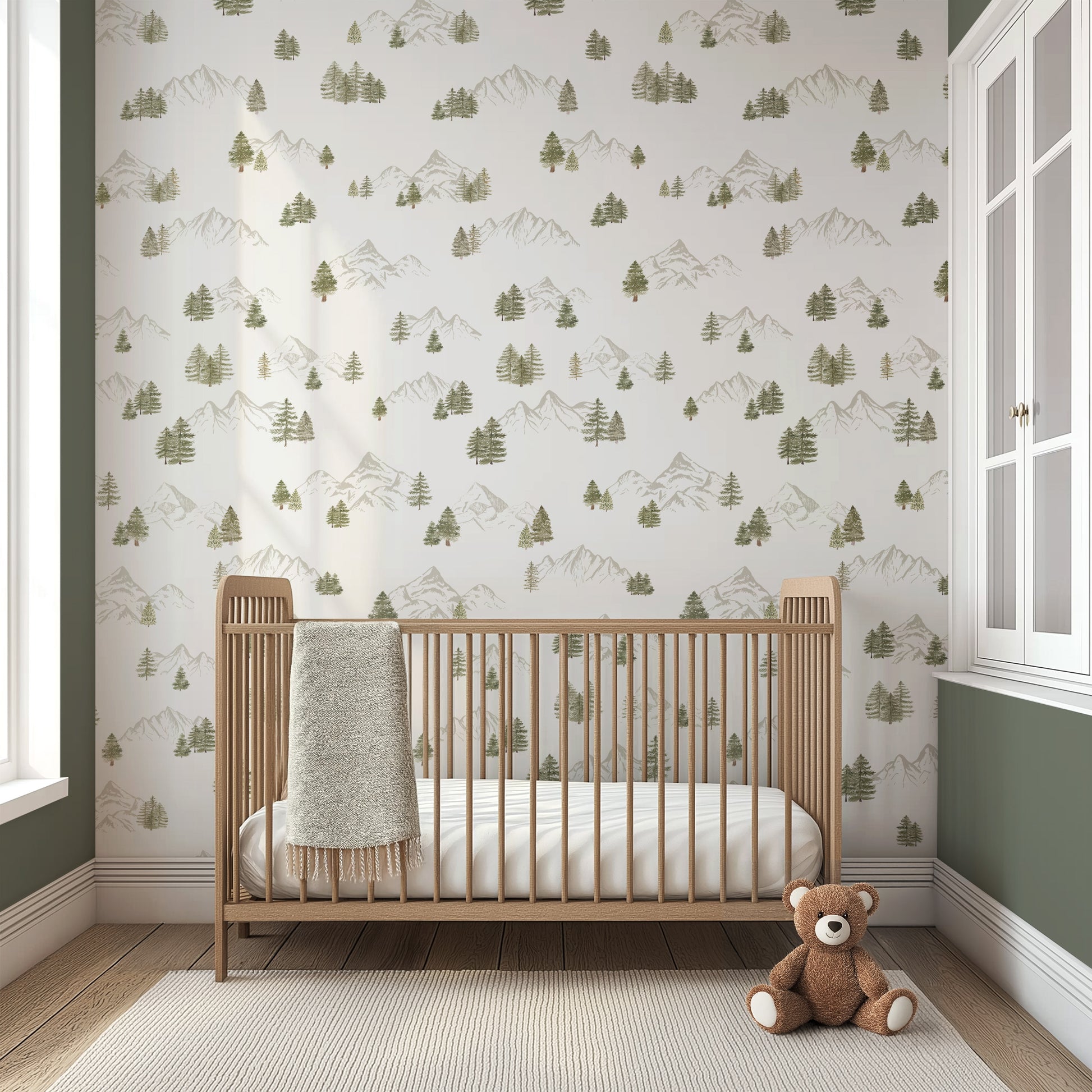 Nursery room with wooden crib and teddy bear against a wall with mountain and tree pattern wallpaper.