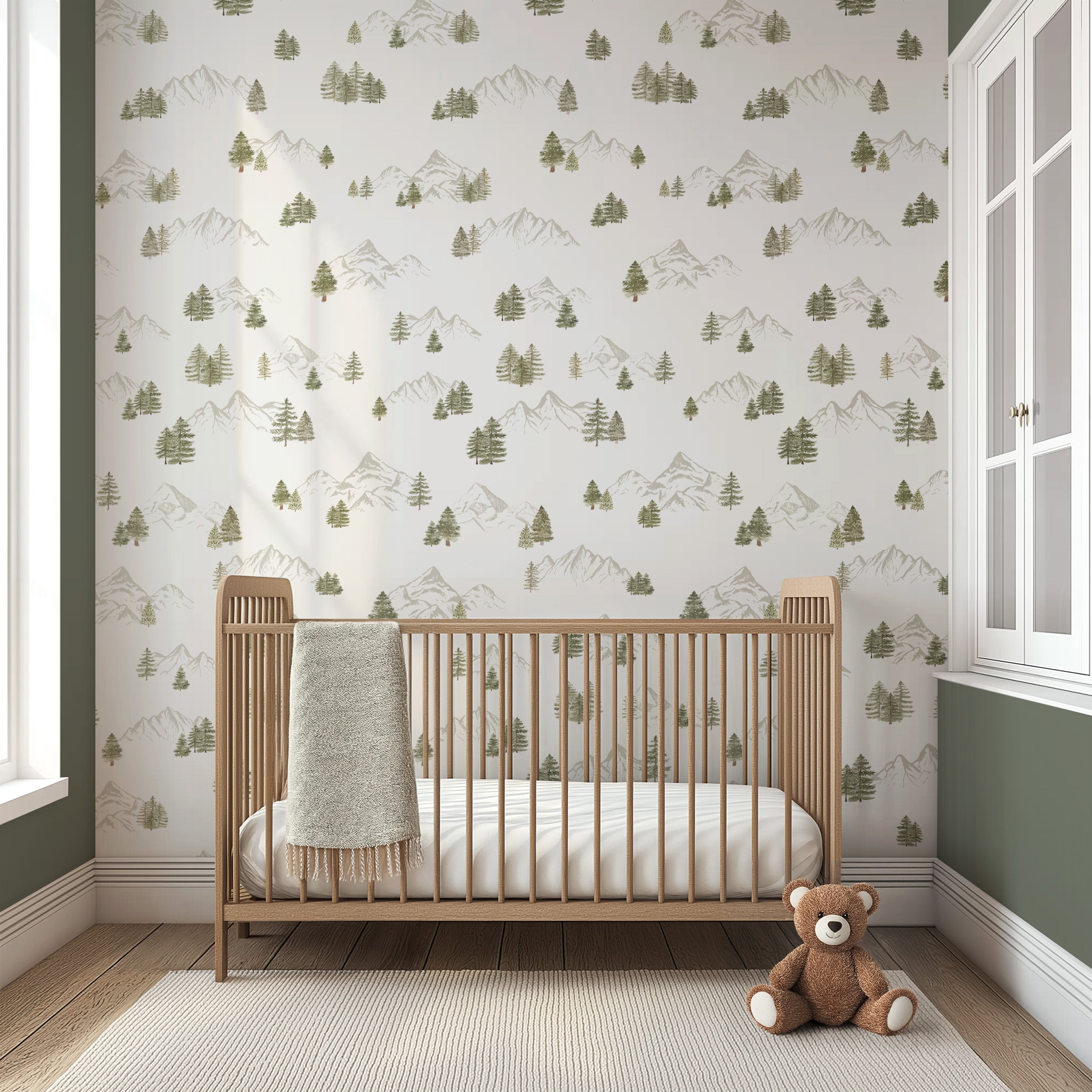Nursery room with wooden crib and teddy bear against a wall with mountain and tree pattern wallpaper.