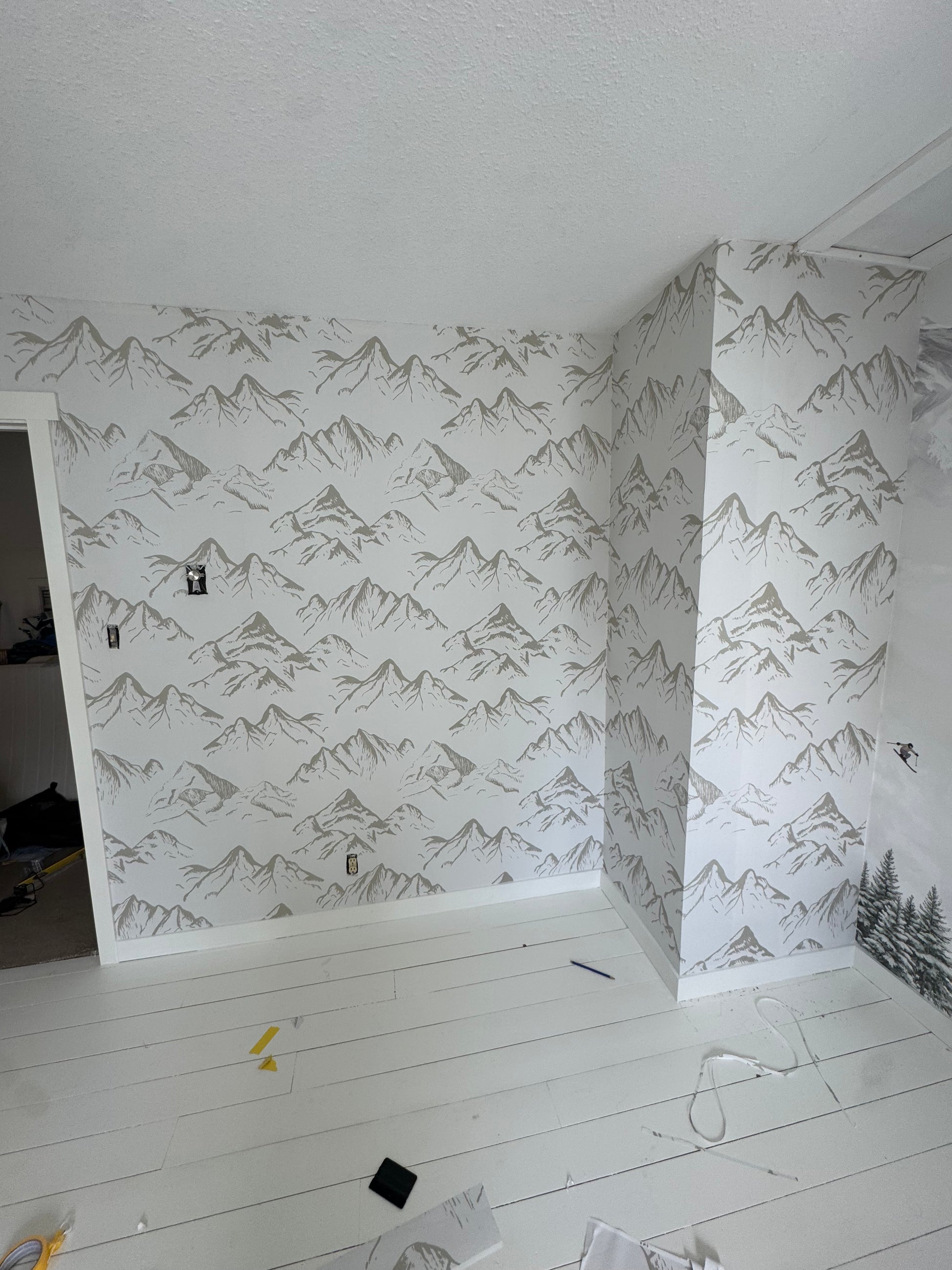 Neutral taupe mountain wallpaper covering a full nursery wall and adjacent column during installation.