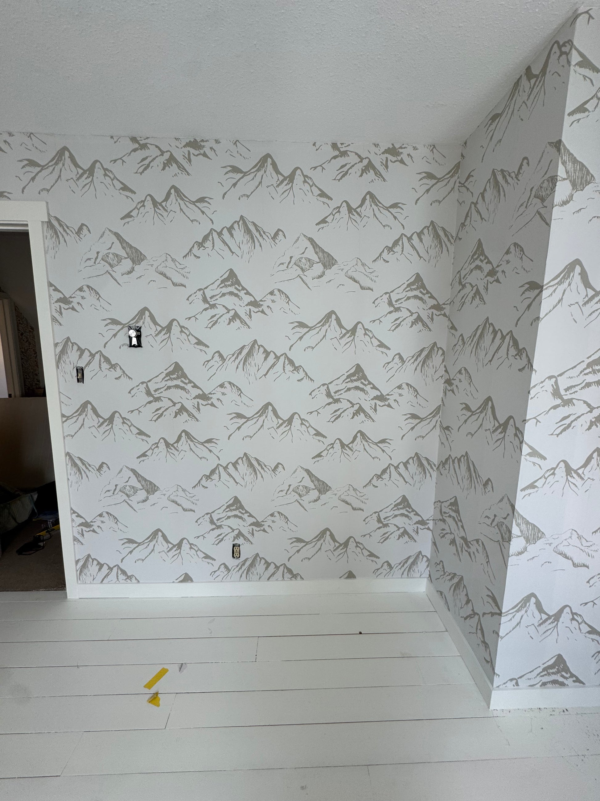 Neutral taupe mountain wallpaper on a clean white nursery wall with bright natural lighting.