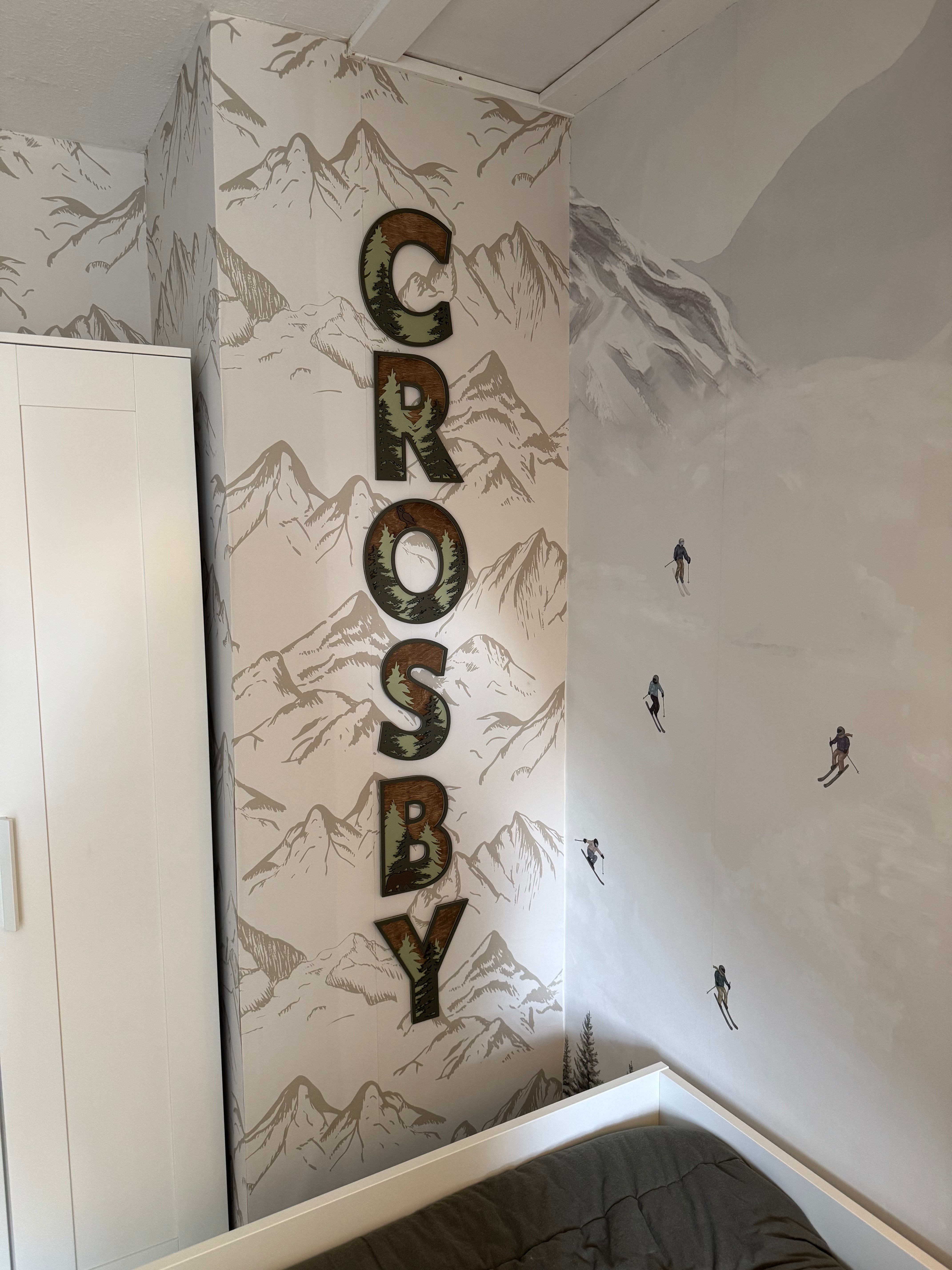 Neutral taupe mountain wallpaper on a column with a custom ‘Crosby’ name sign, next to a watercolor ski mural.