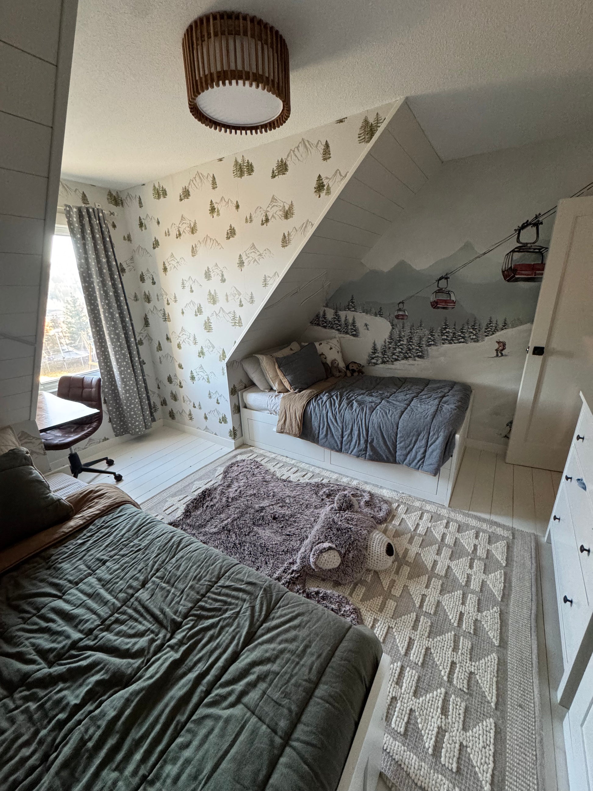 Kids’ room with twin beds featuring the alpine ski mountain mural under the eaves, paired with coordinating mountain wallpaper on the angled wall.
