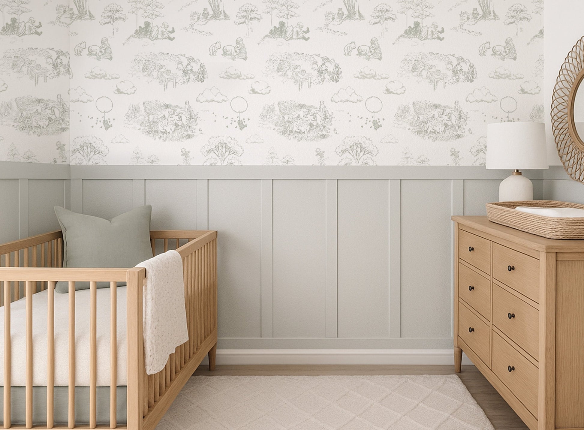 Soft sage Winnie the Pooh toile wallpaper styled above sage wainscoting, shown in a warm nursery with a natural wood crib and dresser.