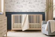 Navy Winnie the Pooh toile wallpaper styled in a soft neutral nursery, with classic line-illustrated woodland scenes behind a light wood crib.