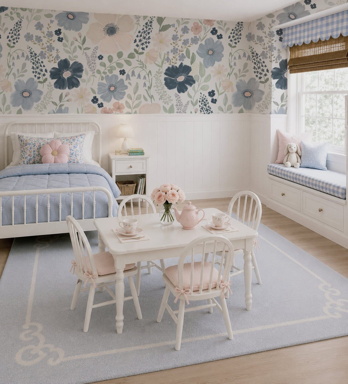 A styled children's bedroom featuring a large scale floral wallpaper accent wall in navy, blue and pink, a white wooden bed, a matching white children's table, four spindle-back chairs with pink cushions, a light blue rug, and a window seat with pillows.