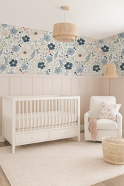 Navy and blush anemone floral wallpaper styled above blush wainscoting in a soft nursery with a white crib and cozy armchair