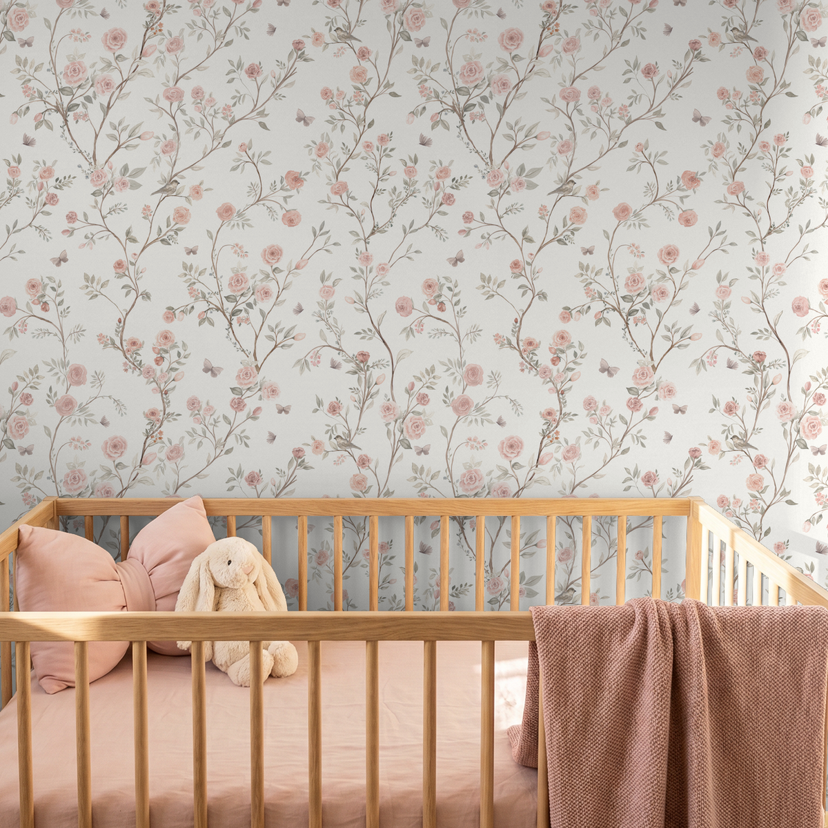 Aurora cream floral wallpaper with climbing pink roses and butterflies behind a natural wood crib with pink bedding.