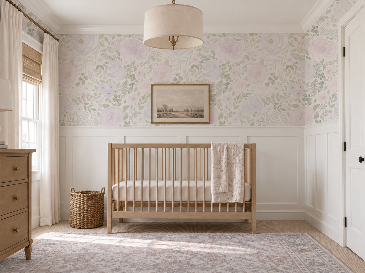Lilac and lavender floral nursery wallpaper with soft watercolor blooms and muted green foliage, paired with white wall paneling, a natural wood crib, warm woven accents, linen curtains, and a vintage-inspired rug.