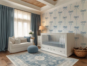 Nursery room with white crib, sofa, and decorative wallpaper featuring blue bows.
