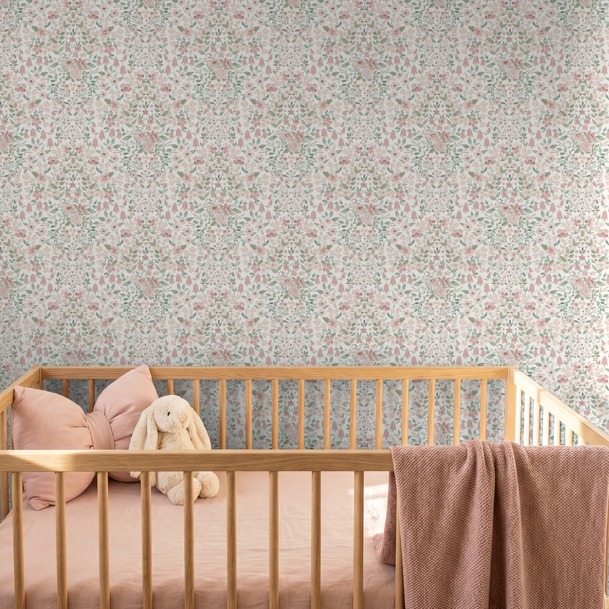 Blush botanical nursery wallpaper paired with natural oak crib and soft plush accents.