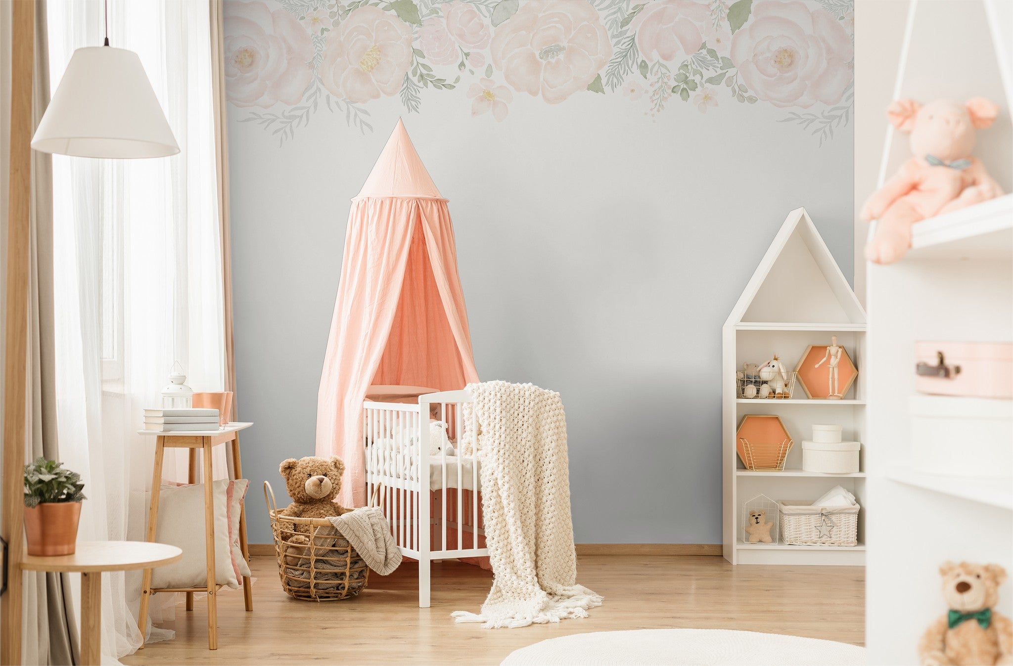 Nursery with soft blush floral border wallpaper and pastel decor.