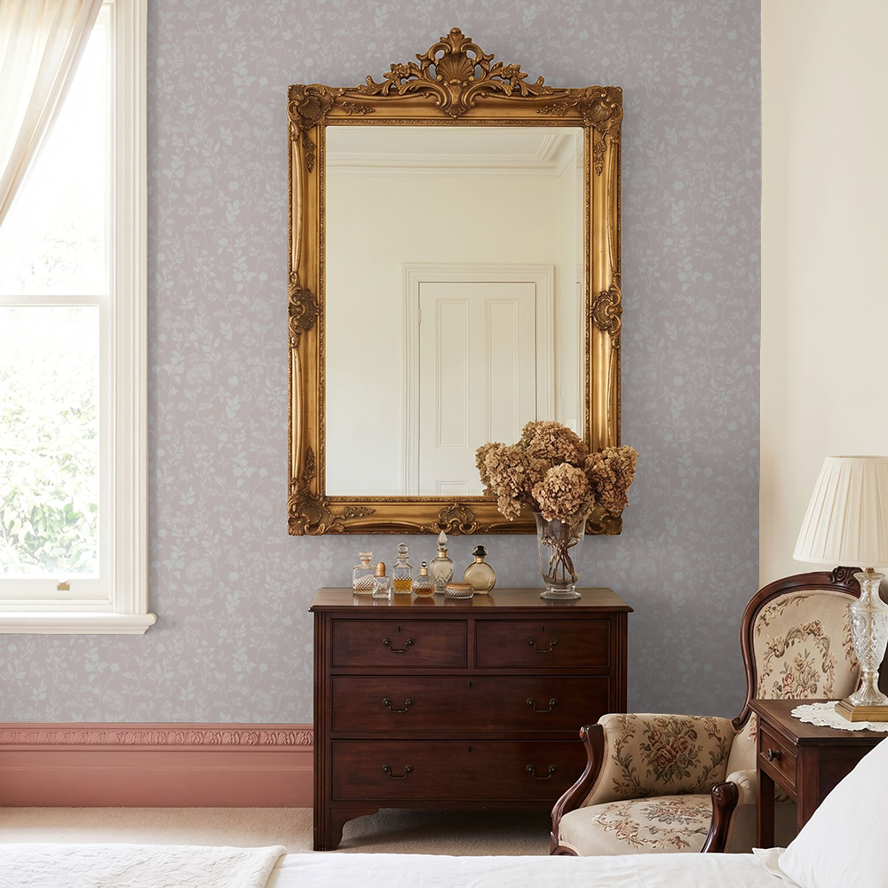 Blush floral wallpaper with vintage mirror in elegant bedroom setting.