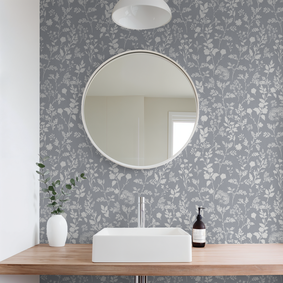 Chambray blue wildflower wallpaper in modern bathroom with round mirror and white sink.