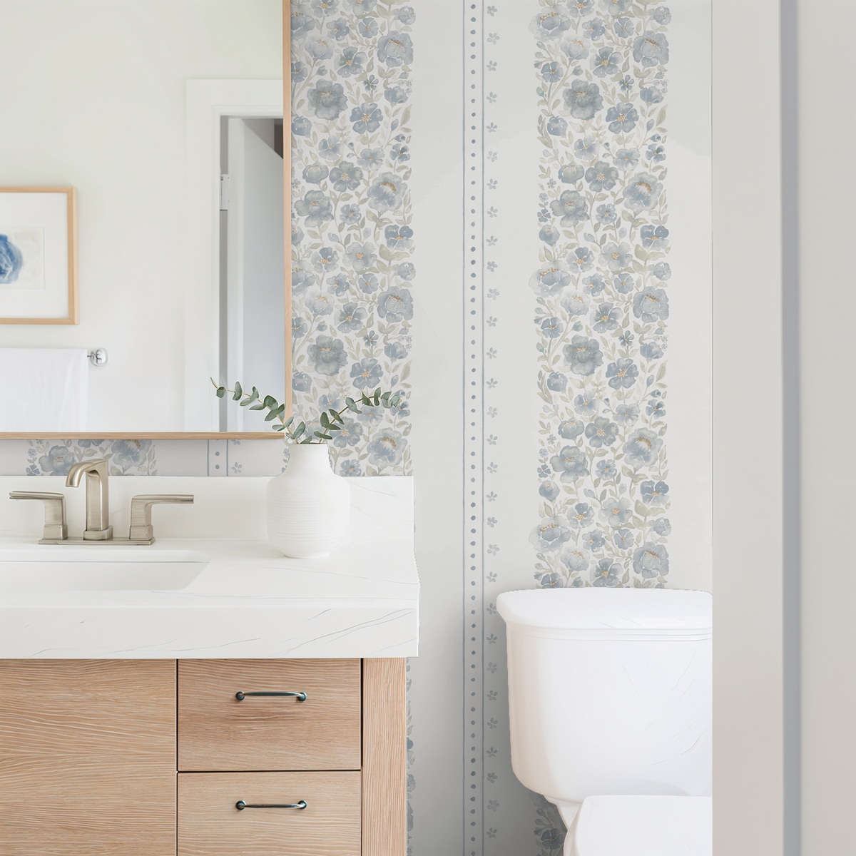 Chambray Cottage blue floral stripe wallpaper in a bright bathroom with light wood vanity, white counter and brass fixtures.