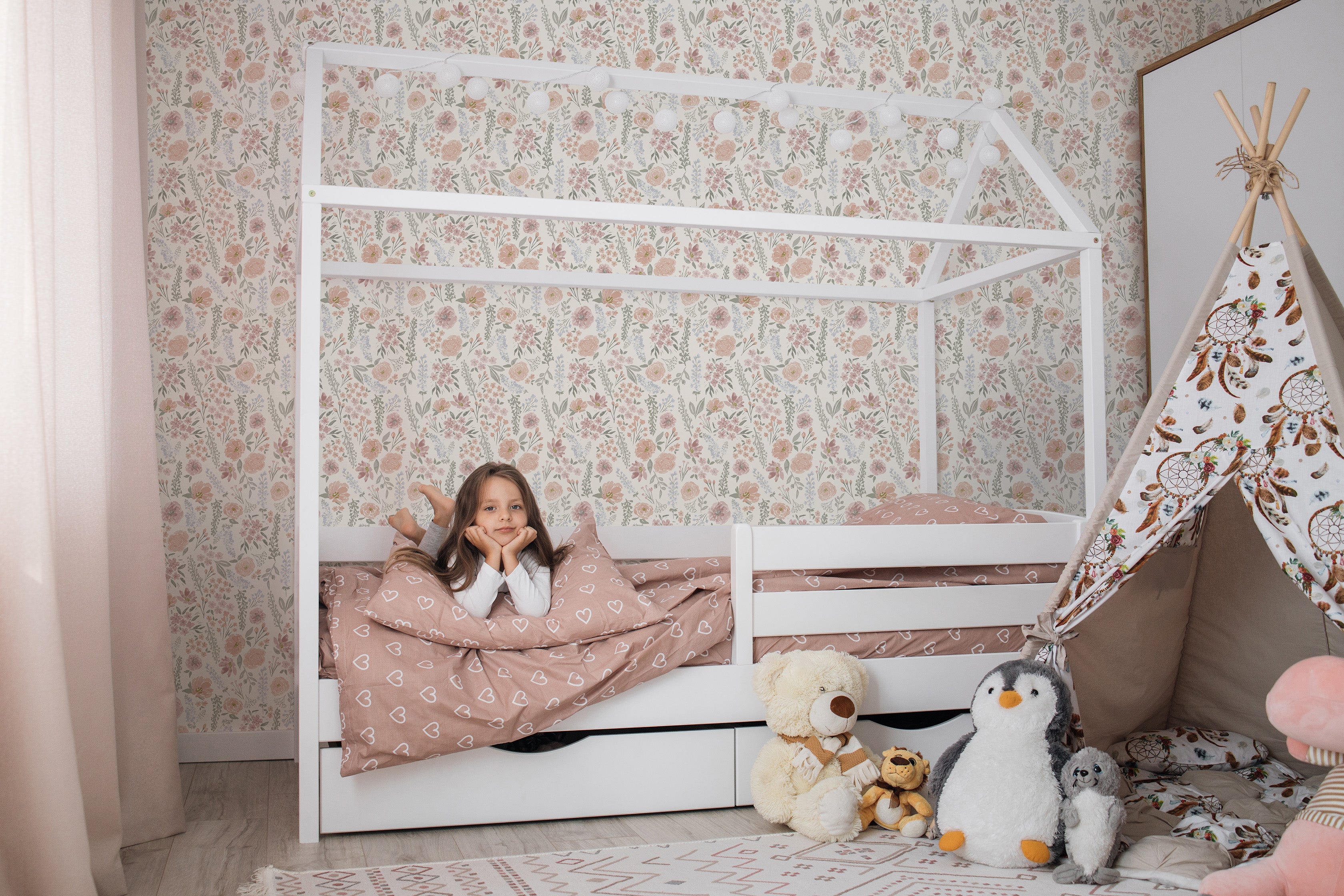 Child in a house shaped bed  in a girls bedroom with vintage floral wallpaper.