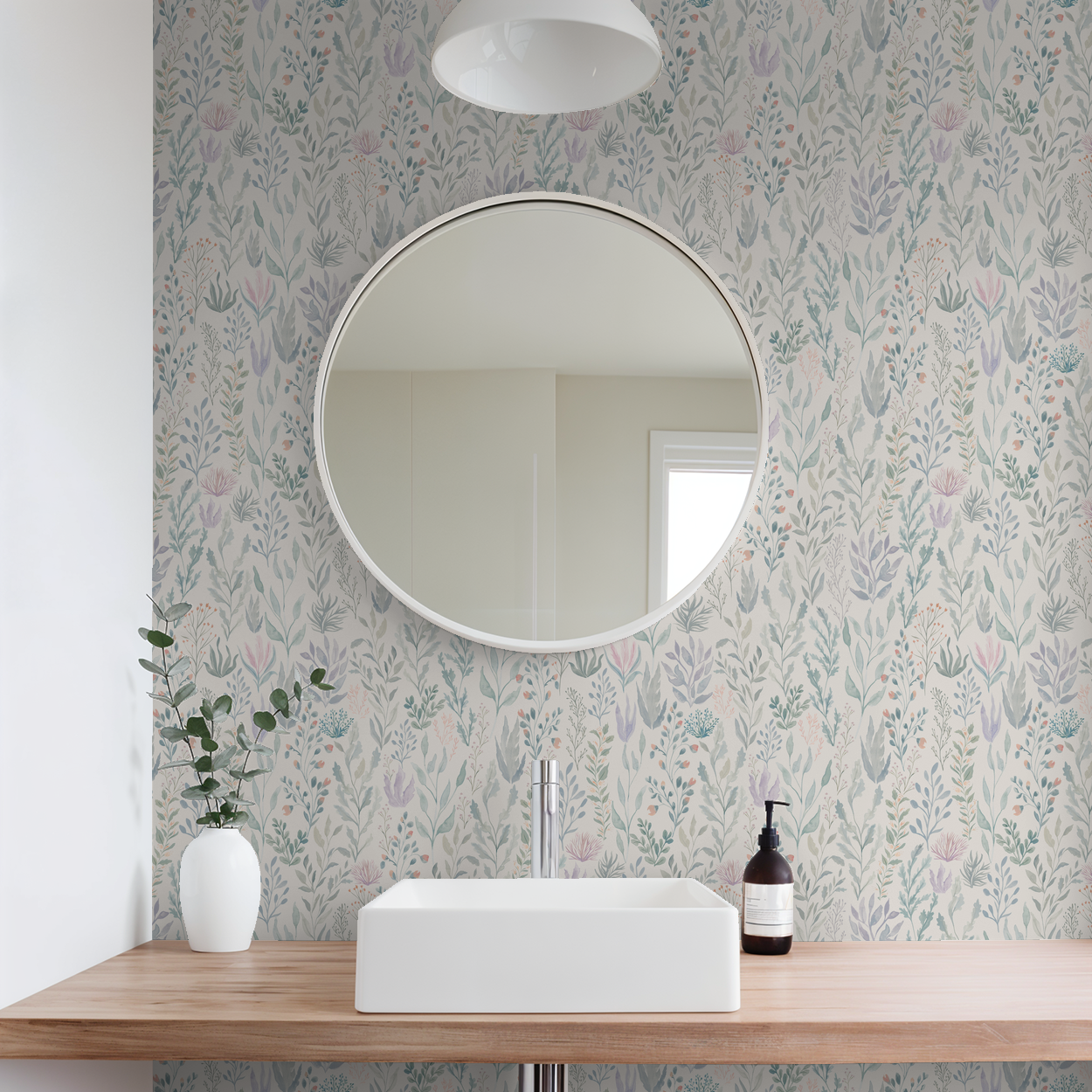 Bathroom with floral reef wallpaper in soft greens and pastels, round mirror, and wooden vanity.