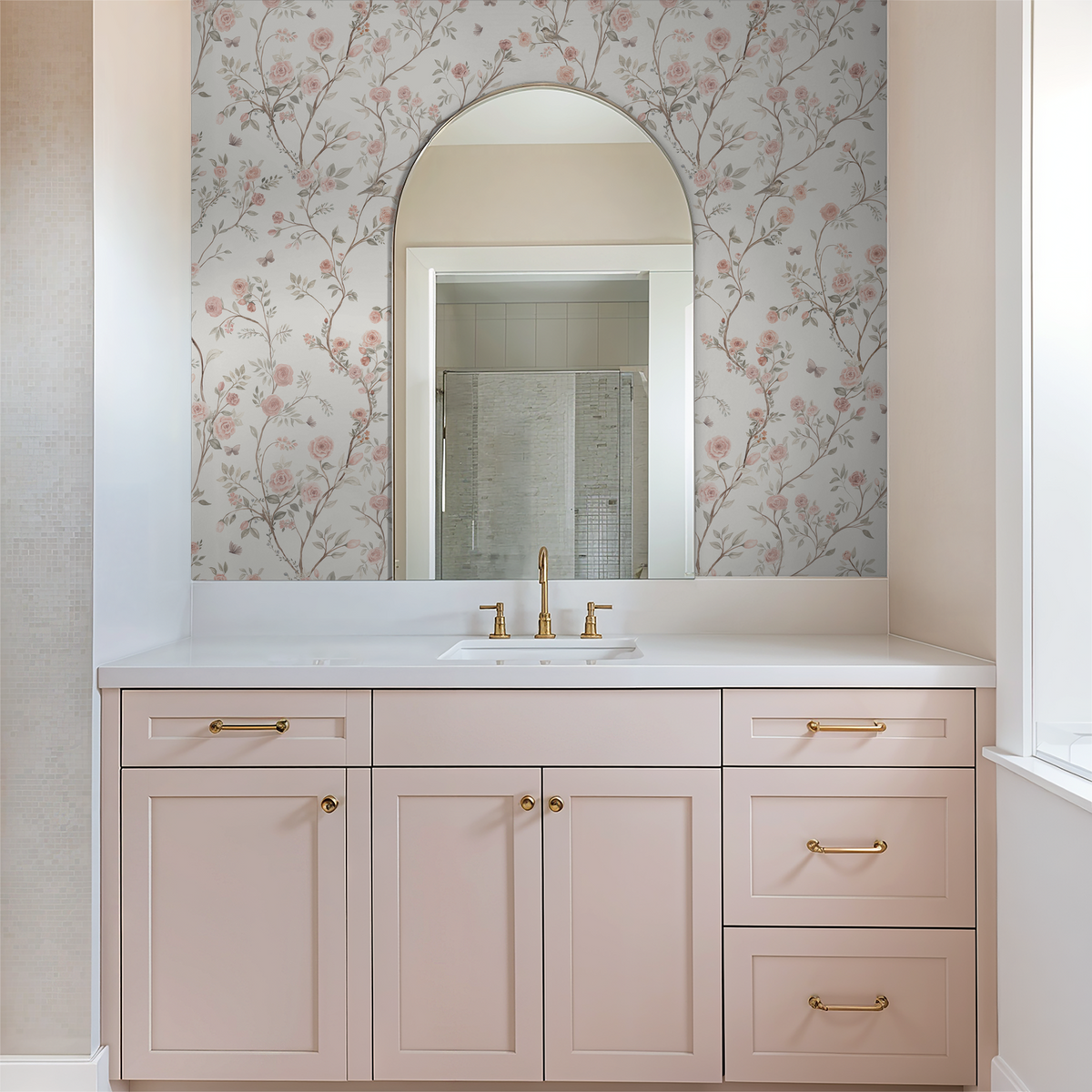Aurora pink rose wallpaper above a blush bathroom vanity with brass hardware and an arched mirror.