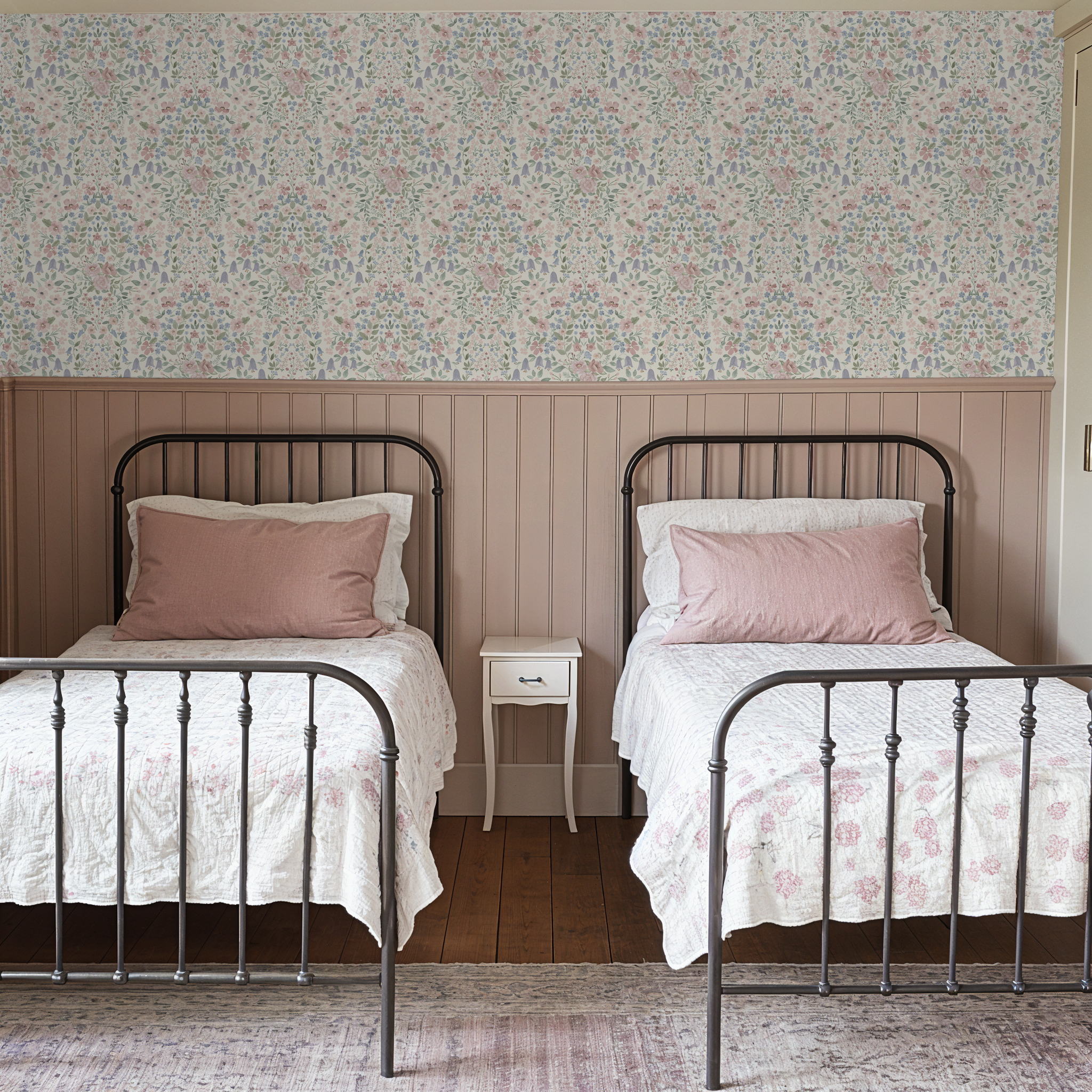 Grandmillennial floral damask wallpaper in a vintage girls bedroom with blush paneling and twin beds.