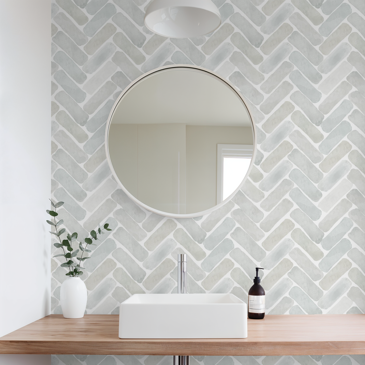 Neutral pottery-inspired watercolor herringbone wallpaper behind a round mirror and minimalist bathroom sink with wood countertop and small vase.