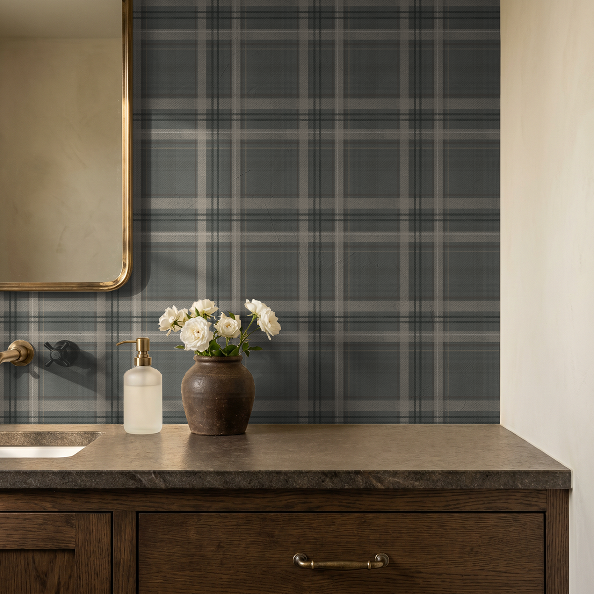 Slate grey-green Lodge Plaid wallpaper behind a bathroom vanity with brass mirror, stone countertop and white flowers.
