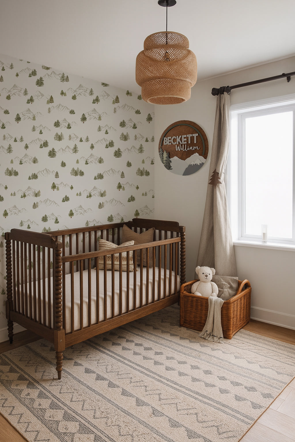 Nursery room with wooden pottery barn crib, forest mountain wallpaper from wildcomb, and a round wooden name plaque with a mountain forest design