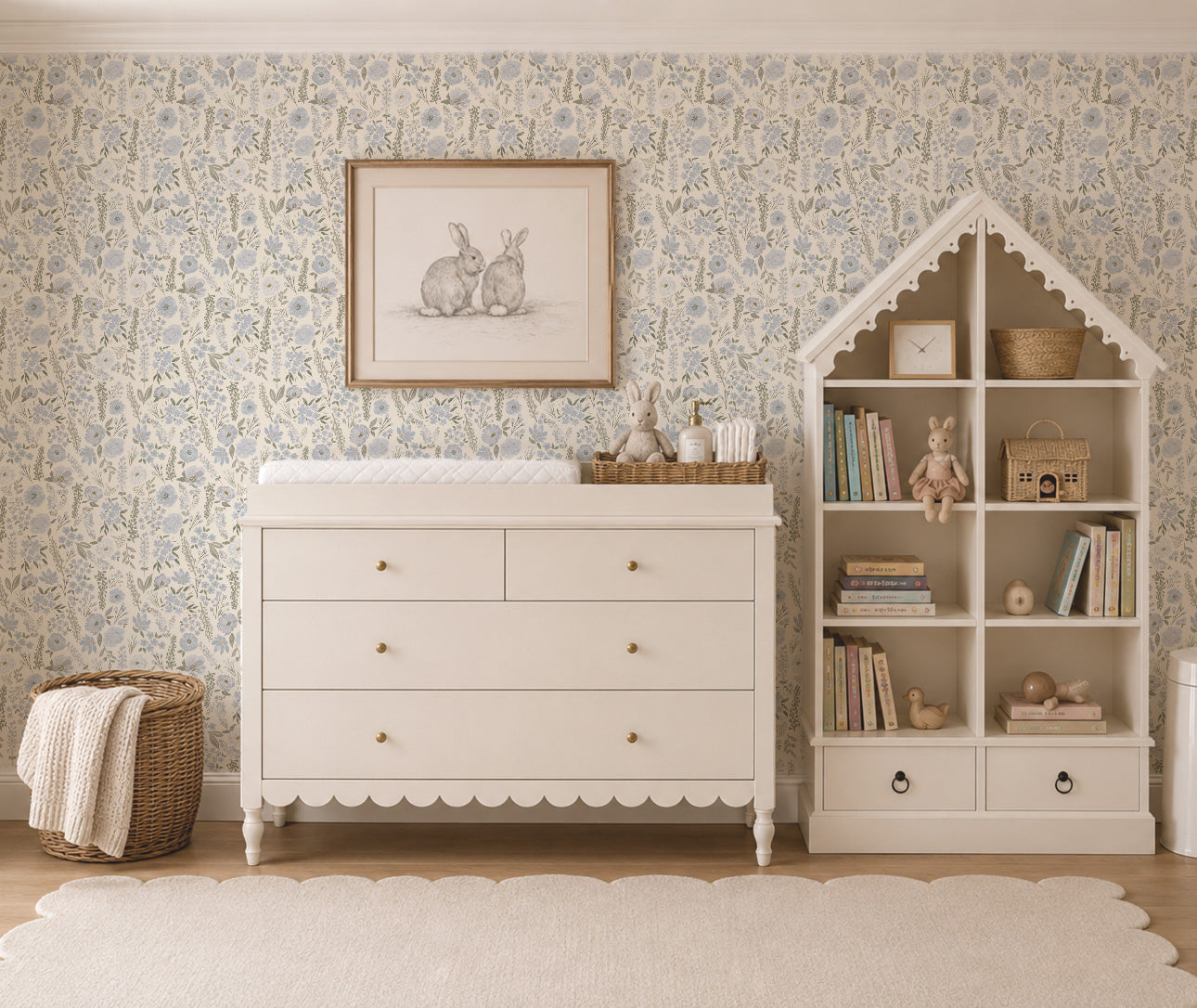 A styled nursery room scene featuring BLue and white floral wallpaper, a white wooden changing dresser and a matching house-shaped bookshelf with decorative books, baskets.