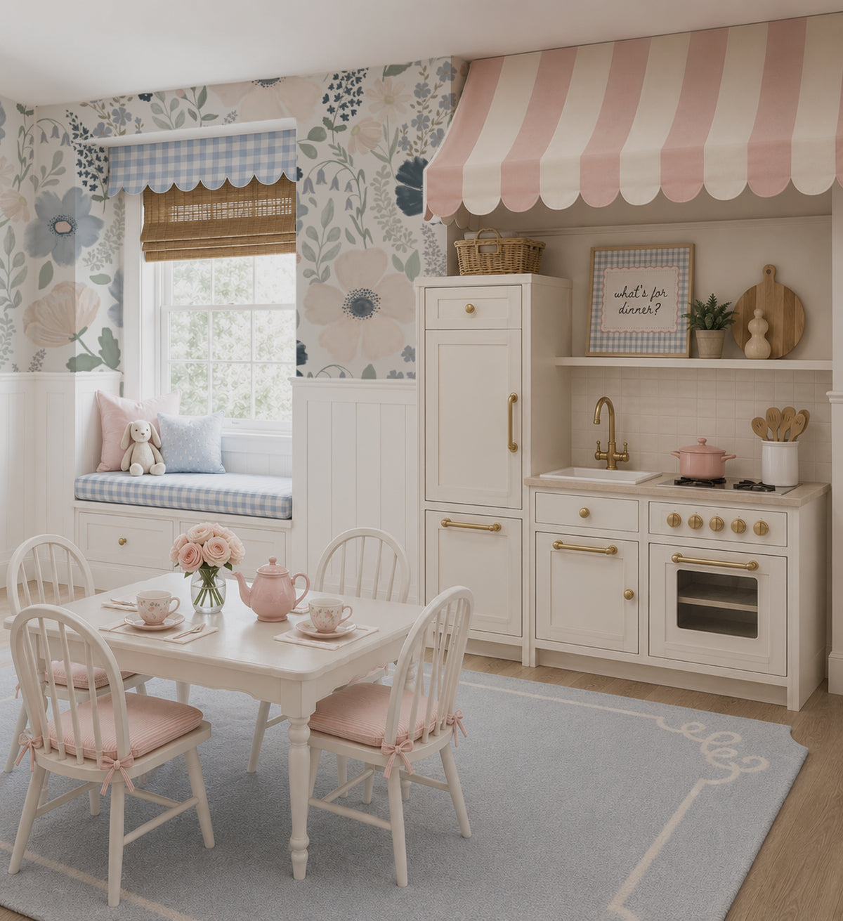 A styled children's play kitchen and dining area set in a bright room with floral wallpaper, a pink-and-white striped awning, a white dining table with four chairs, and a small play kitchen with cream cabinets and gold handles.