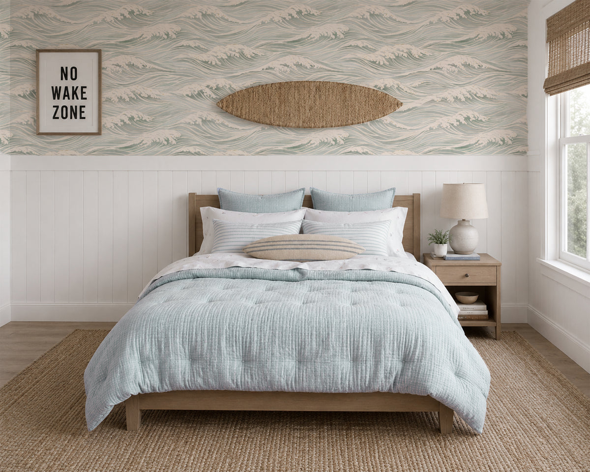 The Waves blue ocean wallpaper above white wainscoting in a relaxed coastal bedroom with natural wood accents.