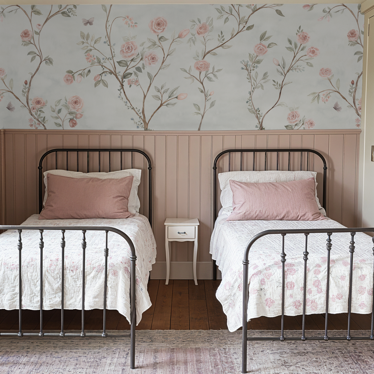 Vintage floral wallpaper with blush roses and botanical branches in a girls' bedroom with twin beds.